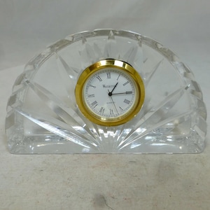 Puede incluir: Un reloj de cristal transparente con una esfera dorada y números romanos. La esfera del reloj dice "Waterston Quartz".