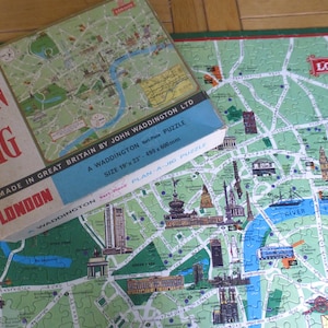 Pode incluir: Um quebra-cabeça vintage de Londres, Inglaterra, com fundo verde e marcos coloridos. A caixa é vermelha, branca e azul com o texto "Plan-A-Jig" e "Londres".
