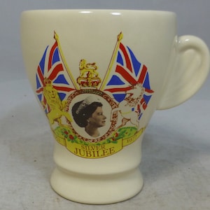 May include: White ceramic mug with a commemorative design for the Silver Jubilee. The design features a portrait of Queen Elizabeth II, two Union Jack flags, a lion and a unicorn, and the text "Silver Jubilee".