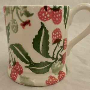 Peut inclure: Une tasse en céramique blanche avec une anse, ornée d'un motif de feuilles vertes et de framboises roses.