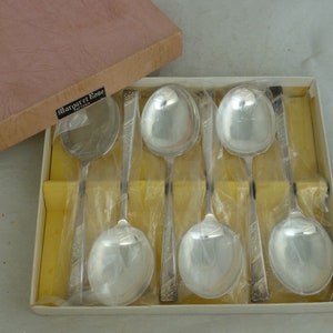 Puede incluir: Un juego de seis cucharas plateadas en una caja. Las cucharas están envueltas individualmente en plástico transparente y tienen un diseño decorativo en los mangos. La caja es de color rosa claro y tiene una etiqueta que dice "Margaret Rose Pattern".