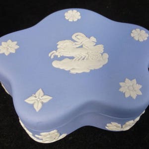 May include: A blue and white ceramic star-shaped trinket box with a raised design of a woman riding in a chariot pulled by a horse. The box is decorated with white floral designs.