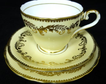 May include: A set of three yellow teacups and saucers with gold trim and floral designs. The cups and saucers are made of fine china and have a delicate, elegant look.