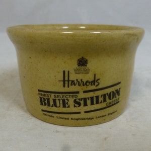 Puede incluir: Un tarro de cerámica beige con una etiqueta negra que dice "Harrods Finest Selected Blue Stilton Cheese Harrods Limited Knightsbridge London England".