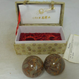 May include: Two brown and grey stone spheres in a velvet-lined box. The box is closed and has a gold and white patterned design. The box lid has a label with the text "中国太原石樓山" in black.
