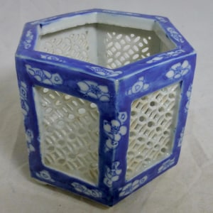 Op de afbeelding: Een zeshoekige keramische vaas met een blauw en wit bloemmotief. De vaas heeft een traliewerkpatroon aan de zijkanten en is blauw afgewerkt. De binnenkant is wit.