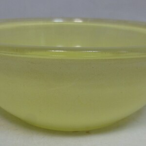 May include: A pale yellow glass mixing bowl. The bowl is round and has a smooth, glossy finish.