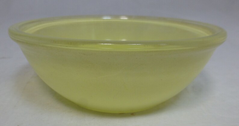 May include: A pale yellow glass mixing bowl. The bowl is round and has a smooth, glossy finish.