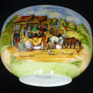 May include: A vintage ceramic bowl featuring a colourful illustration of a horse-drawn carriage and people in a town setting. The bowl has a green and yellow glaze and the words "Dickens' Days" are printed on the bottom.