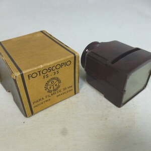 May include: A brown cardboard box with the text "FOTOSSCOPIO FS-35 PARA FILMS DE 35 MM INDUSTRIA BRASILEIRA" and a logo. Next to the box is a dark brown plastic film viewer.