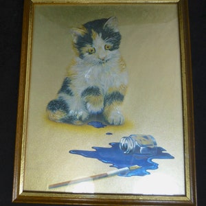 Puede incluir: Una impresi&oacute;n enmarcada de un gatito calico sentado sobre un fondo dorado con un frasco de tinta azul derramado y un pincel.
