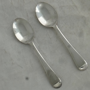 May include: Two silver teaspoons with rounded bowls and long, slender handles.