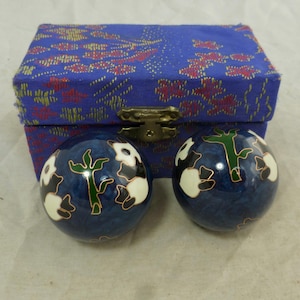 May include: Two spherical metal balls with a deep blue enamel finish, featuring white and black panda bear designs and green bamboo stalks outlined in gold. The pair is presented in a rectangular blue fabric-covered box with a metal latch.