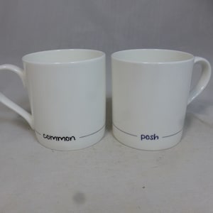 Puede incluir: Dos tazas de cerámica blanca con líneas negras y texto escrito a mano. La taza de la izquierda dice "common" y la taza de la derecha dice "posh".