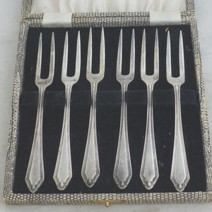 May include: Set of six silver-plated cake forks in a black velvet lined box. The forks have a decorative design and are in excellent condition.