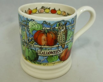 May include: A white ceramic mug with a Halloween theme. The mug features a blue and green background with a pumpkin, an owl, and the word "HALLOWEEN" on a sign.