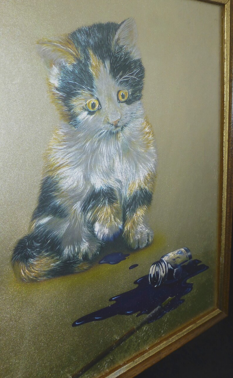 Puede incluir: Un gatito calico con pelaje negro, blanco y naranja se sienta sobre un fondo dorado. El gatito est&aacute; mirando hacia abajo a una botella de tinta azul derramada.