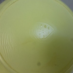 May include: Close-up of the bottom of a pale yellow ceramic bowl with the letters "KDA" embossed in the center.