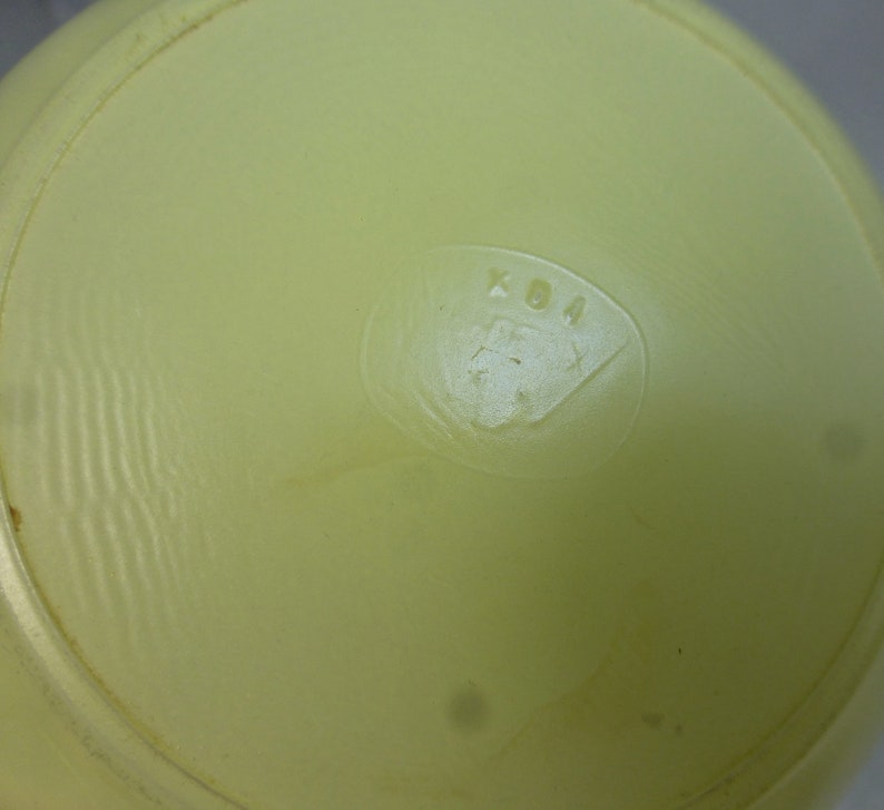 May include: Close-up of the bottom of a pale yellow ceramic bowl with the letters "KDA" embossed in the center.