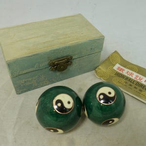 May include: Two spherical green meditation balls featuring black and white yin-yang symbols, accompanied by a light blue fabric-covered storage box with a brass latch and a small instructional paper card labelled Iron Ball Direction.