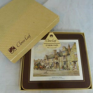 May include: A set of six brown and white table mats featuring a vintage illustration of a building with a sign that reads "The Bell Inn, Stilton". The mats are packaged in a brown box with the Clover Leaf logo and the text "Clover Leaf 6 table mats Made in United Kingdom".