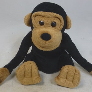 May include: A black and brown plush monkey toy sitting with its arms outstretched. The monkey has a brown face with black eyes and a black nose.