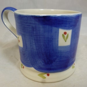 May include: A blue ceramic mug with a white rim and handle. The mug has a white and blue patterned design with green leaves and red berries.