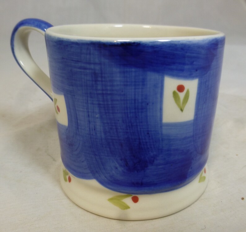 May include: A blue ceramic mug with a white rim and handle. The mug has a white and blue patterned design with green leaves and red berries.