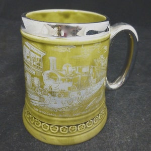 May include: A green ceramic mug with a silver rim and handle. The mug features a white image of a steam locomotive with the text "GW 1400 CLASS No. 1420 DART VALLEY RAILWAY".