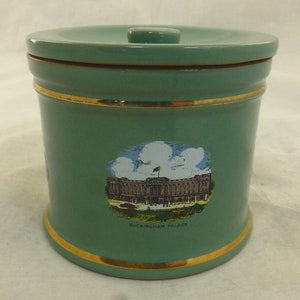 May include: A green ceramic jar with a gold lid and a gold band around the top and bottom. The jar has a picture of Buckingham Palace on the front with the text "Buckingham Palace" underneath.