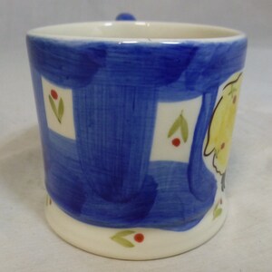May include: A blue and white ceramic mug with a yellow and white painted design. The mug has a white rim and base.