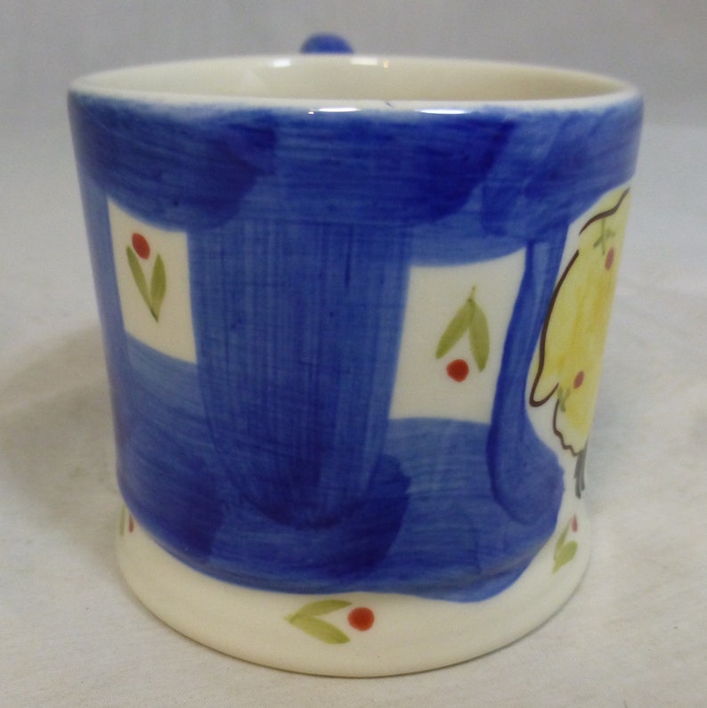 May include: A blue and white ceramic mug with a yellow and white painted design. The mug has a white rim and base.