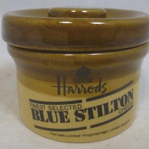 May include: A brown ceramic jar with a lid, featuring the Harrods logo and the text "Finest Selected Blue Stilton Cheese". The jar also includes the text "Harrods Limited Knightsbridge London England".