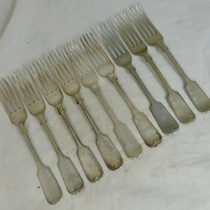 May include: A collection of eight silver forks arranged diagonally. Each fork has four tines and a long, slender handle. The handles have a rounded end with a decorative design. The forks are displayed on a white surface.