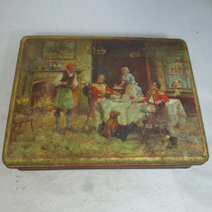 Puede incluir: Caja de hojalata vintage con una ilustración colorida de un grupo de personas reunidas alrededor de una mesa en una habitación con una chimenea. La escena representa una reunión formal con un perro y una mujer sirviendo.