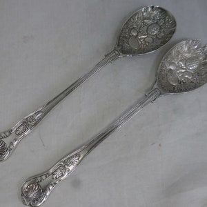 Puede incluir: Un juego de dos cubiertos para ensalada de plata con mangos ornamentados y un diseño decorativo de frutas y hojas en las superficies de servicio.