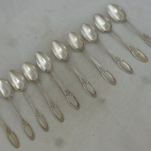 May include: A set of ten silver teaspoons with ornate handles. The spoons are arranged in a row on a white surface.