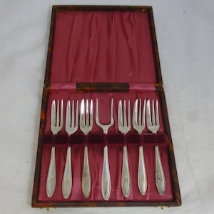 May include: A set of eight silver cake forks in a brown wooden box with a red velvet lining.