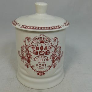 Könnte beinhalten: Cremefarbener Keramiktopf mit Deckel, verziert mit einem roten Design und dem Text "Fortnum & Mason Est 1707 Stilton with Port". Der Topf hat eine runde Form und einen kleinen Knopf auf dem Deckel. Geeignet für Lebensmittel.
