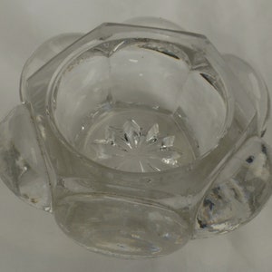 Puede incluir: Un salero de vidrio transparente con base hexagonal y un diseño en forma de estrella en la parte inferior.