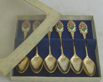 May include: Set of six gold-tone teaspoons with floral designs on the handles. The spoons are in a box with a blue velvet lining.