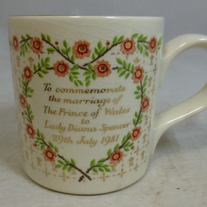 Może przedstawiać: Biały kubek ceramiczny z złotym wzorem kwiatowym i tekstem "To commemorate the marriage of The Prince of Wales to Lady Diana Spencer 29th July 1981".