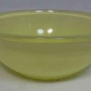 May include: A yellow glass mixing bowl with a smooth, rounded interior. The bowl is made of a translucent material and has a slightly frosted finish.