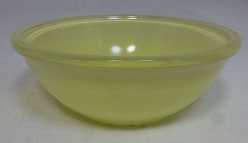 May include: A yellow glass mixing bowl with a smooth, rounded interior. The bowl is made of a translucent material and has a slightly frosted finish.