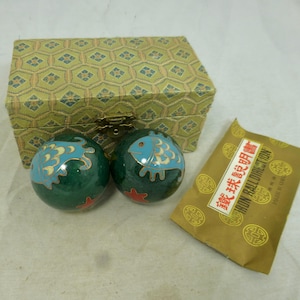 May include: Two spherical metal balls with a dark green enamel finish, featuring light blue fish designs with gold-tone outlines and small red starfish accents. They are accompanied by a rectangular fabric-covered box and an instruction card.
