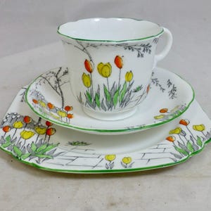 Puede incluir: Juego de té blanco con taza, platillo y plato con diseño floral de tulipanes. El juego presenta tulipanes amarillos y naranjas con hojas y tallos verdes. Los bordes son festoneados y ribeteados en verde.