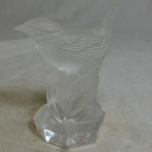 Puede incluir: Una escultura de pájaro de cristal esmerilado. El pájaro está posado sobre una base estilizada, con patrones detallados de plumas y alas. La escultura tiene una apariencia clara y translúcida y es probablemente un artículo decorativo.