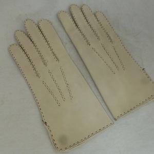 May include: A pair of off-white leather gloves with stitched detailing. The gloves have a simple design and are made of a soft, supple leather.