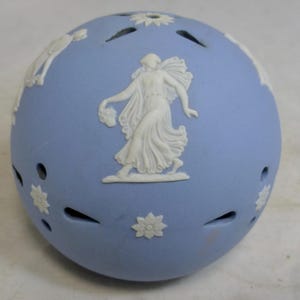May include: A pale blue ceramic sphere with white relief detailing. The sphere is adorned with a central figure of a woman in flowing robes, surrounded by floral and classical designs. There are evenly spaced decorative cutouts.