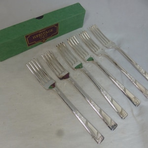 May include: Six silver forks with a decorative pattern, in a green box with the text "Heritage Plate" on the top.